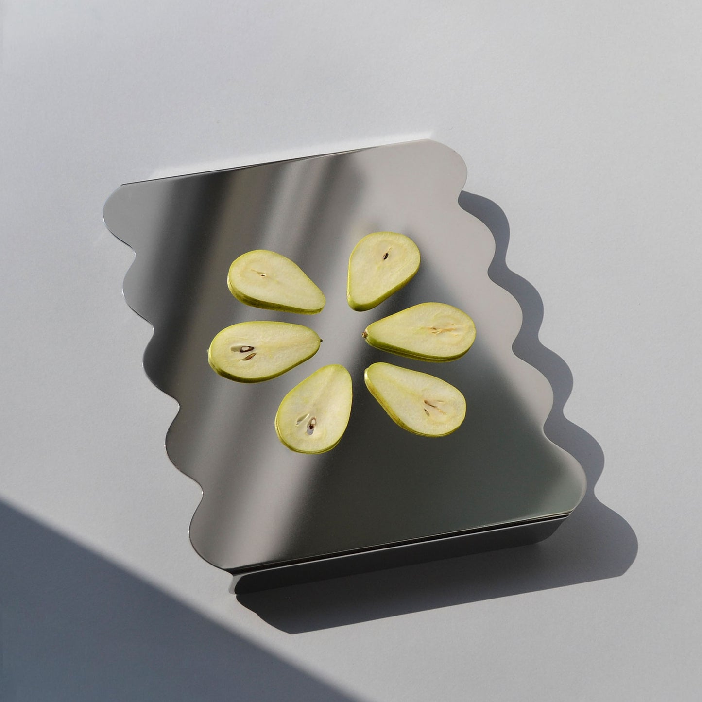 Sliced pears on a modern wavy stainless steel serving stand with reflective surface