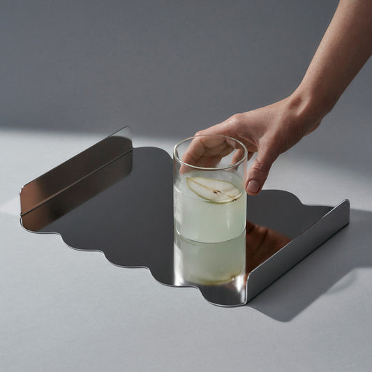 Top side view of the stainless steel sculptural tray with reflecting surface and a cocktail with pear