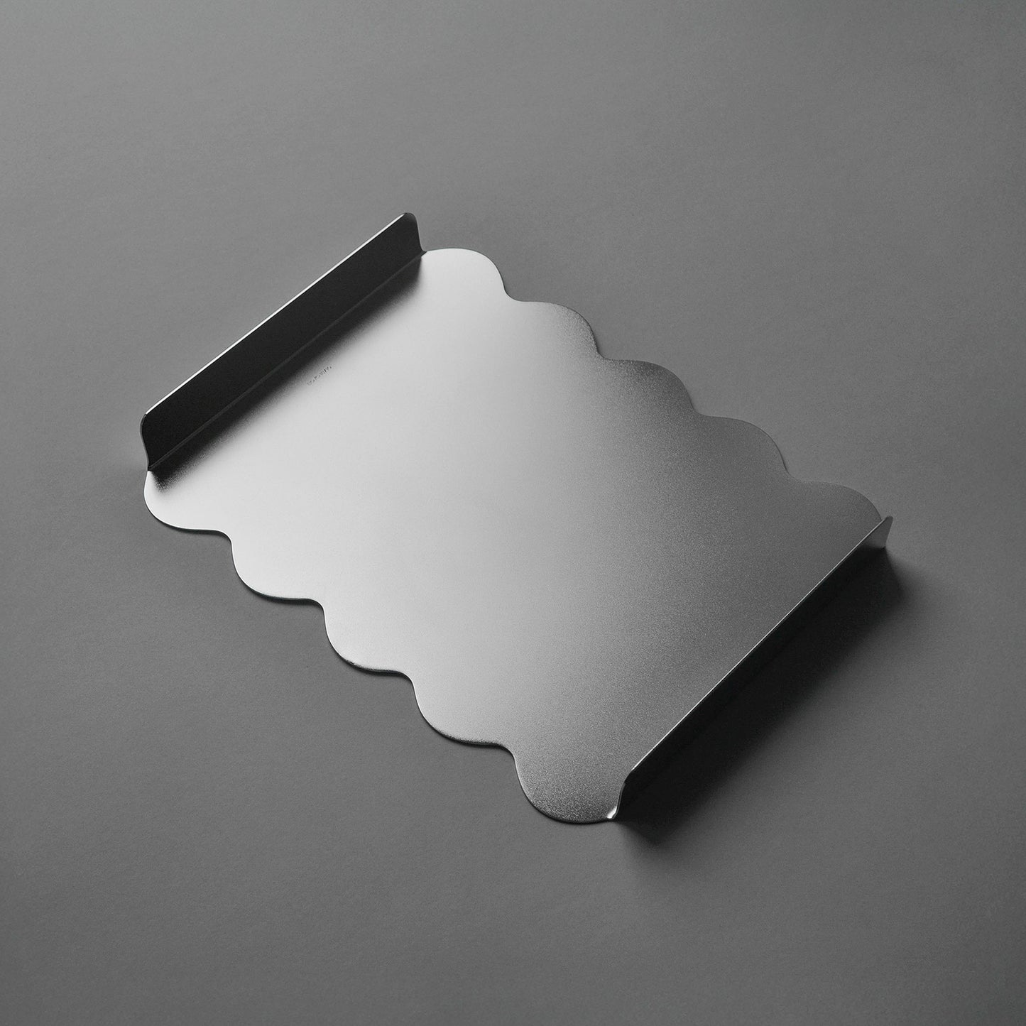 Stainless steel tray with wavy edge on a gray background and softly reflecting surface