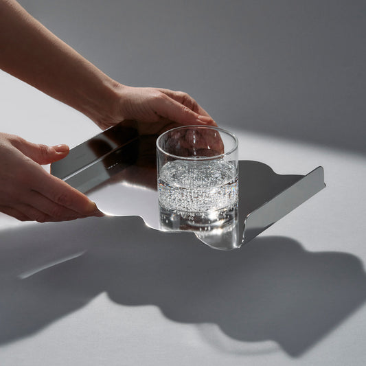 Person holding a mirror sculptural stainless steel tray and a glass of sparklink water