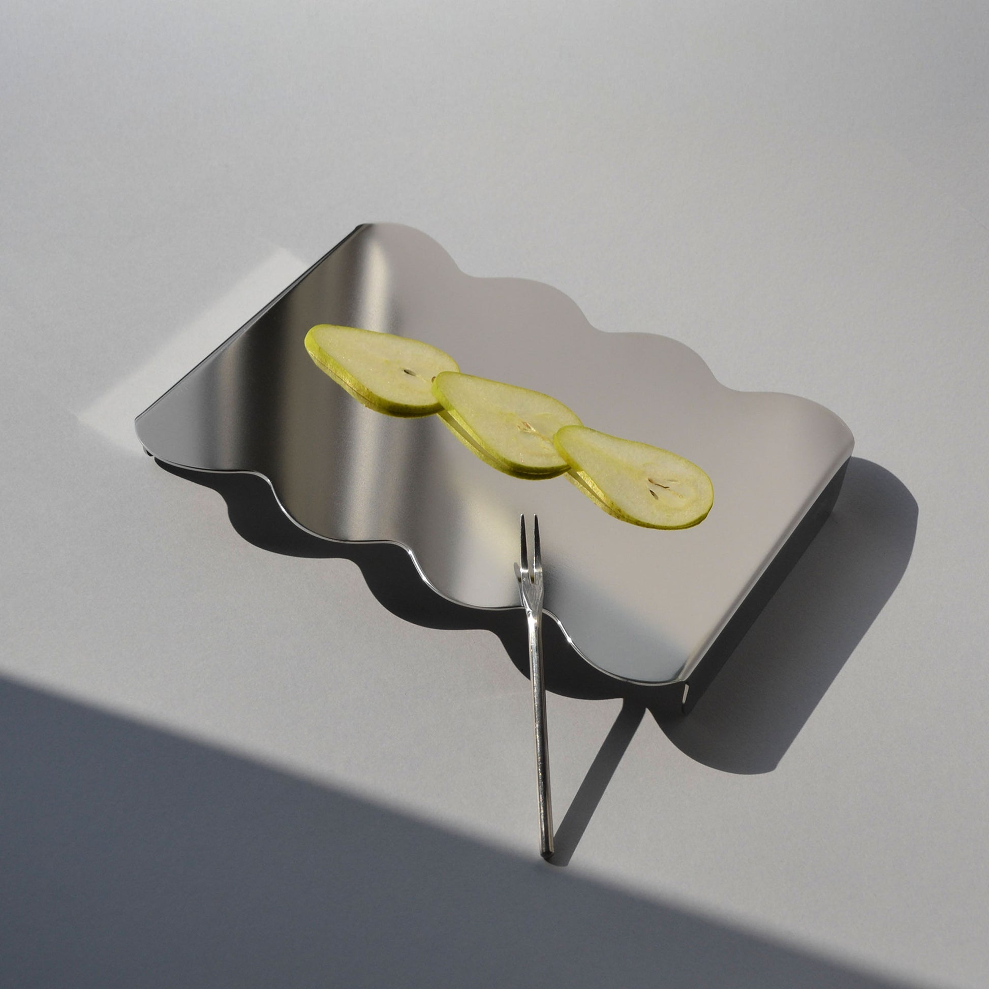 Top view of a modern serving stand with reflective finish and sliced pears on top 
