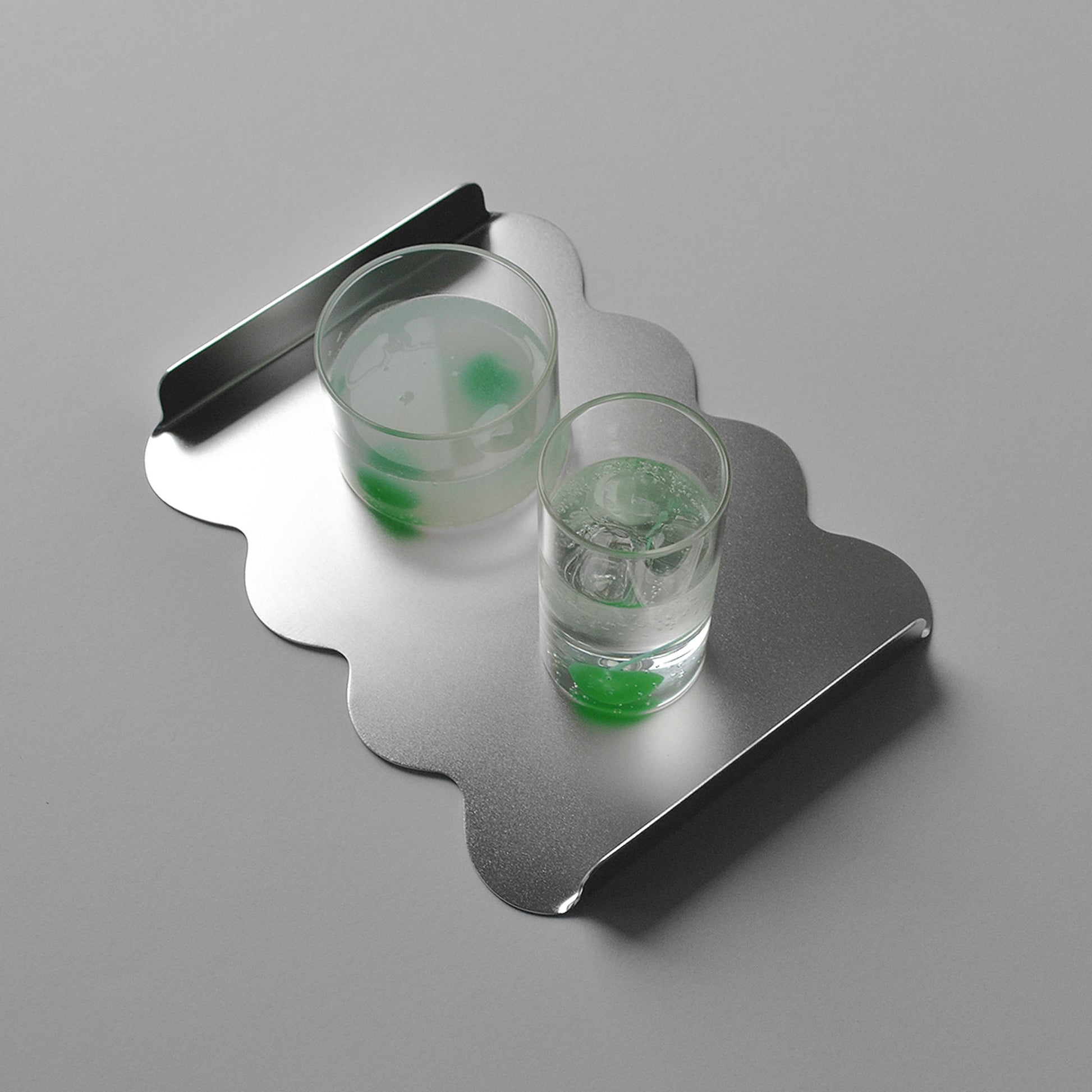Wavy modern tray in stainless steel with two glasses and green cherries inside