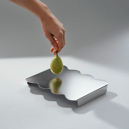 Hand holding a pear aobve the stainless steel modern serving stand