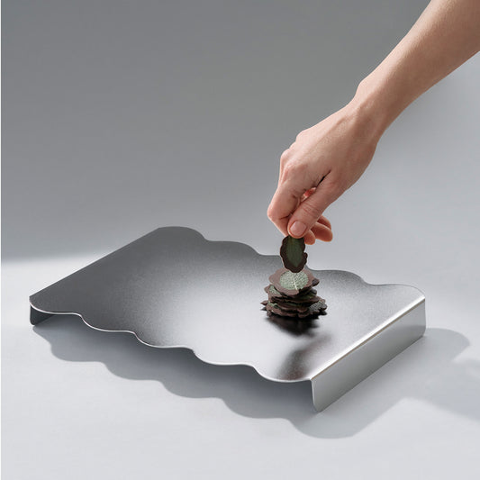 Hand placing a mint choclate on a wavy stainless steel serving stand with a soft matt finish