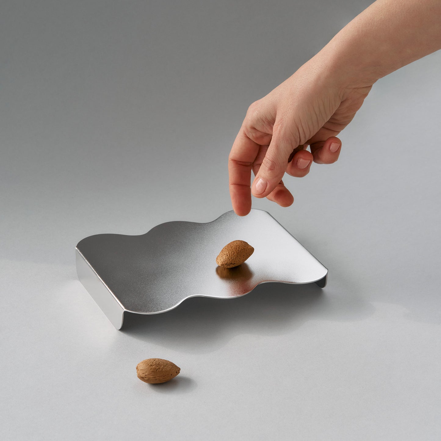 Top view of a hand with almonds and sculptural serving stand in stainless steel soft matt finish