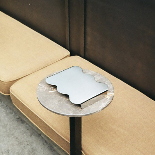 A small round side table with a circular gray stone top and black metal pedestal base, holding a silver wavy-edged tray.