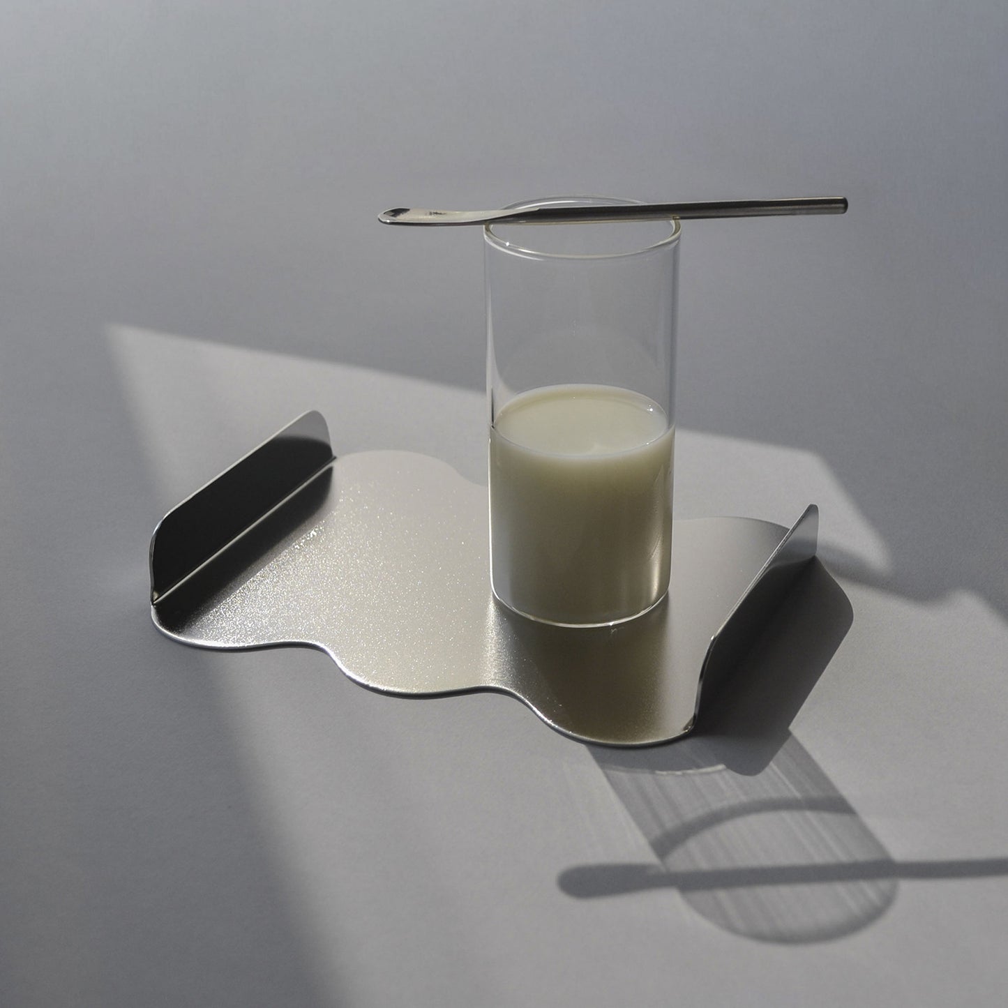 Glass of milk on a sculptural serving tray with satin finish and a small spoon