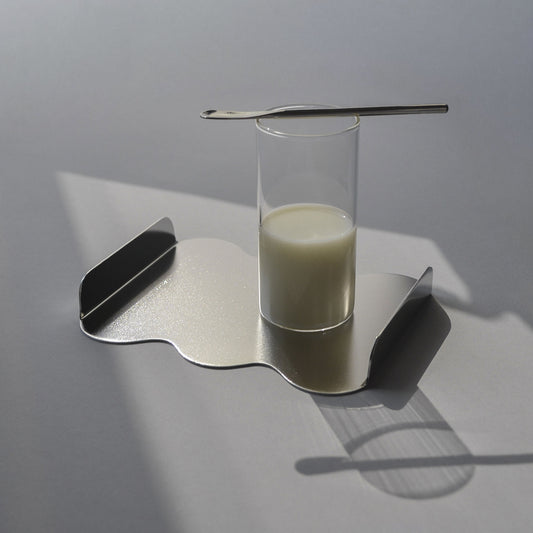 Glass of milk on a sculptural serving tray with satin finish and a small spoon