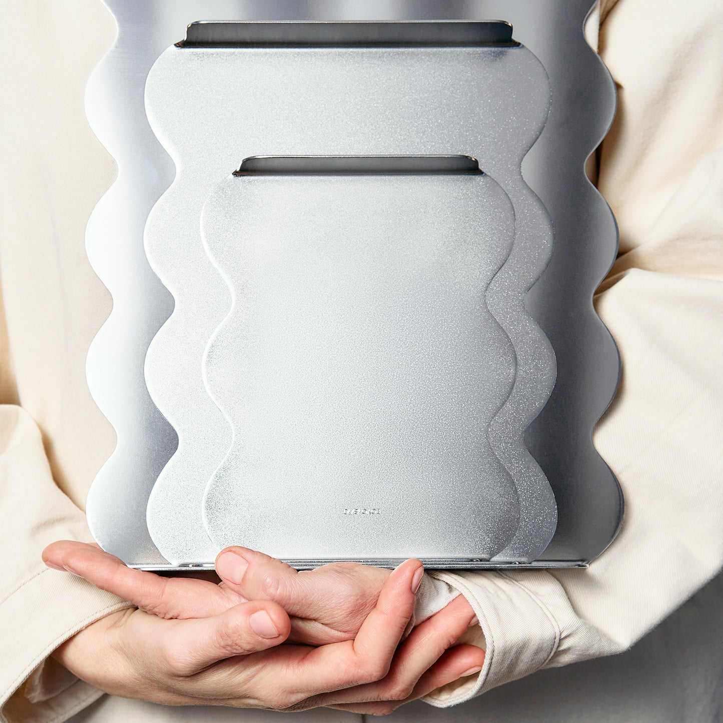 Person holding a modern, wavy-patterned  set of serving trays in stainless steel