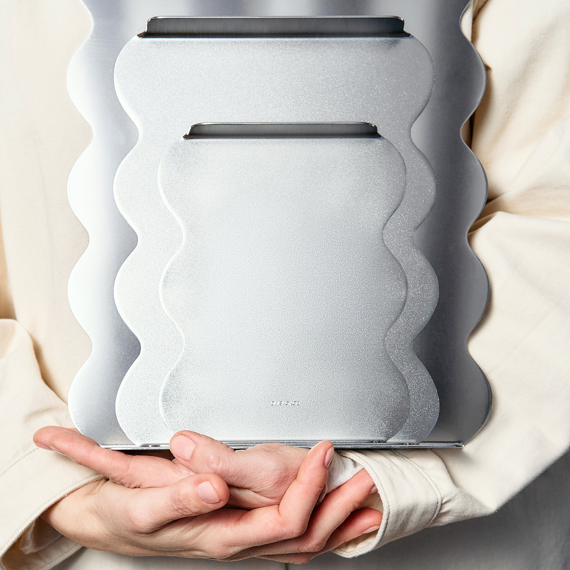 Person holding a modern, wavy-patterned  set of serving trays in stainless steel