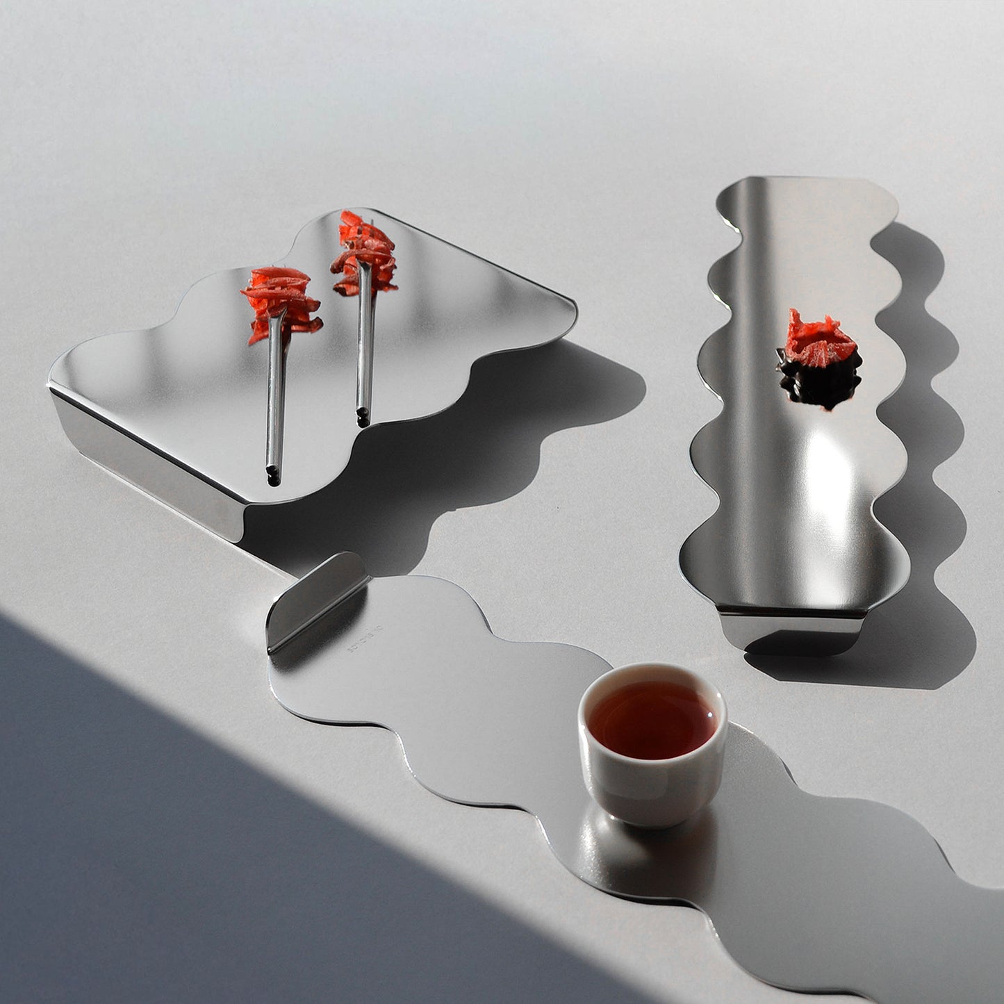 Sculptural serving stands and trays on a grey backround with red food and drink on top